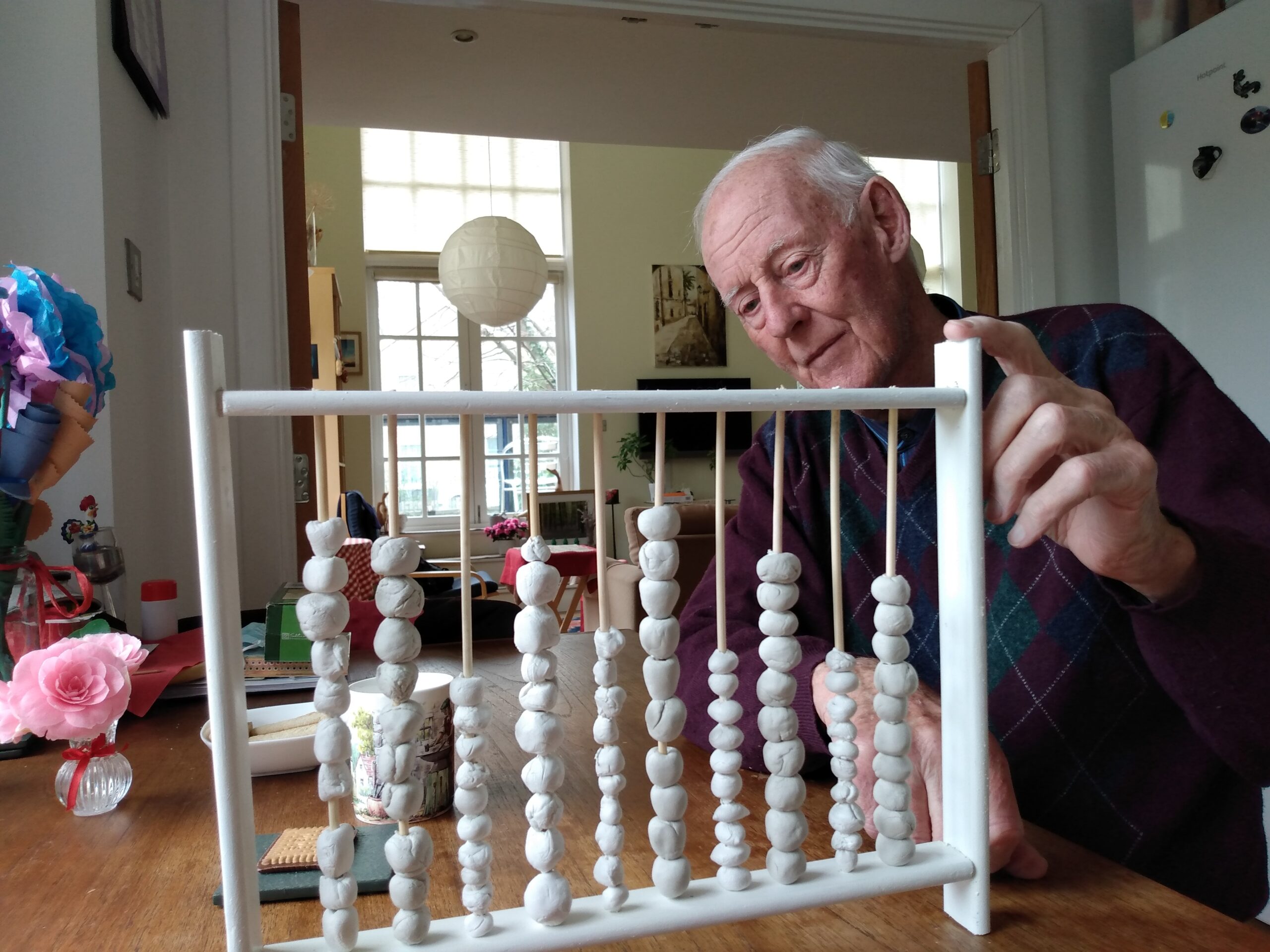 a man sits at a table in his living room, behind a sculpted clay abacus