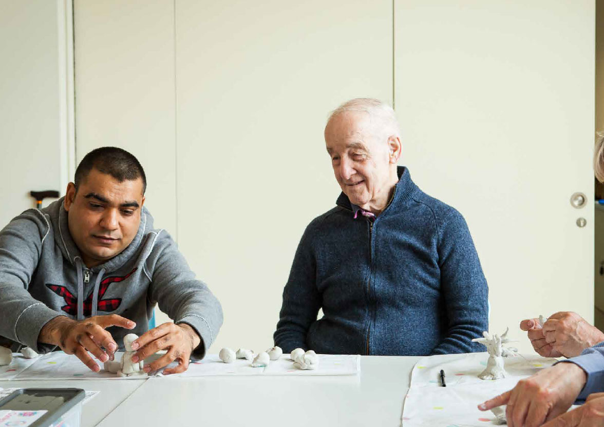 A group of people are sitting around a table. They are making small sculptures out of clay.