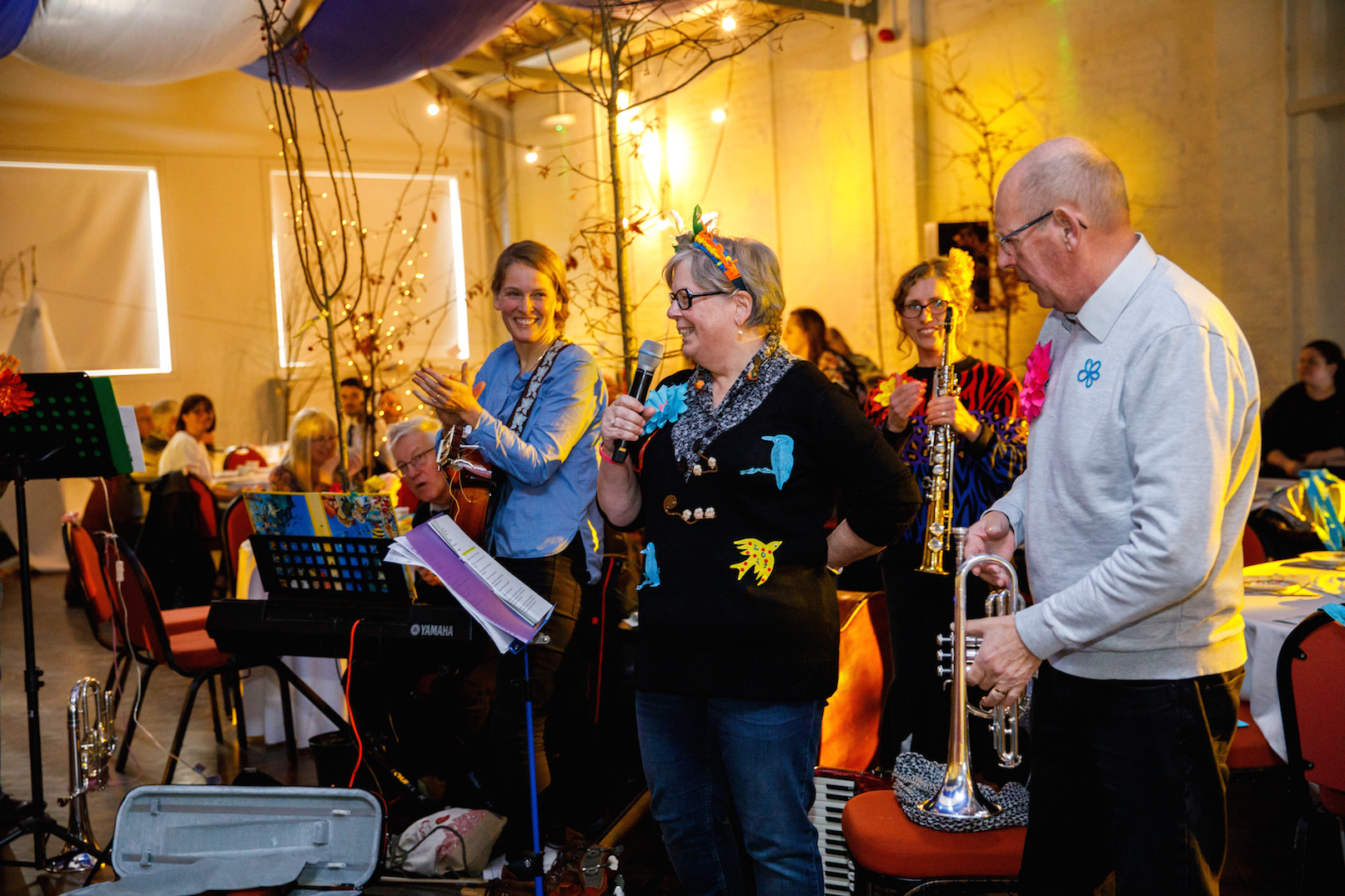 A group of people sing and play instruments in a crowded room with a celebratory atmosphere