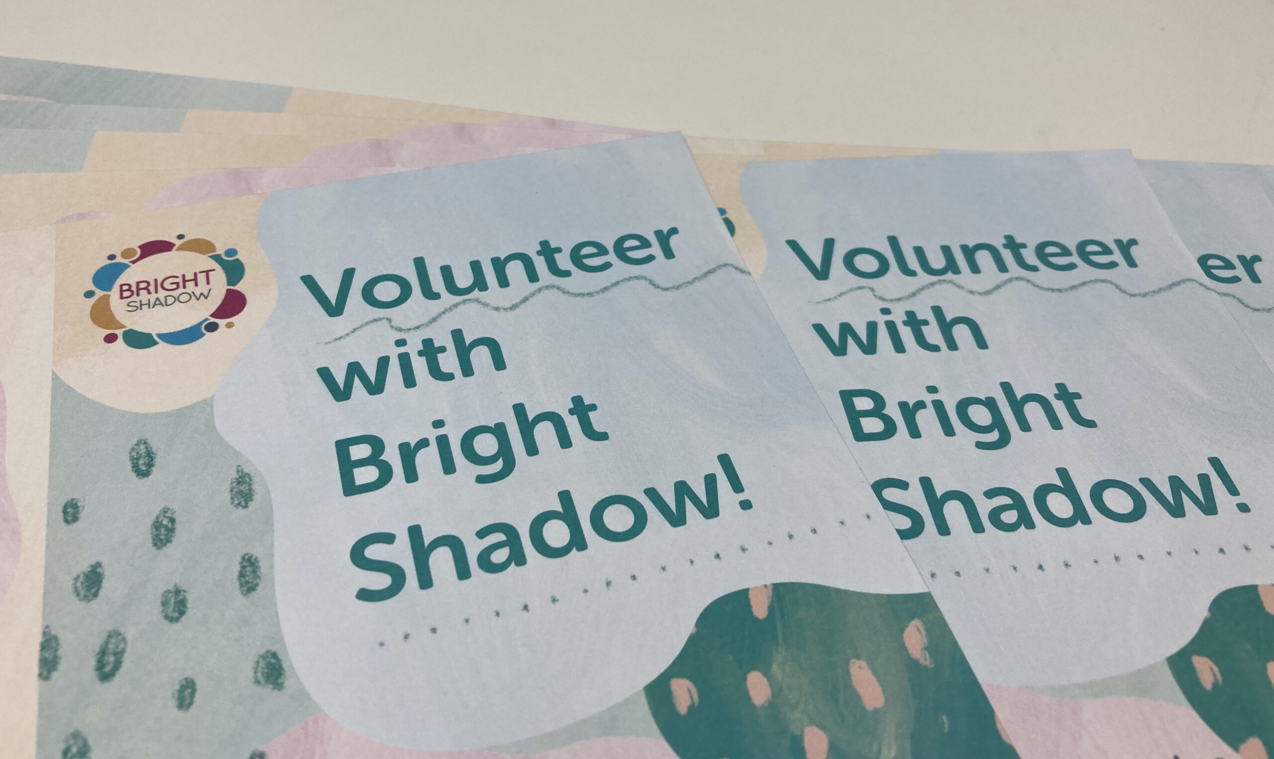 Volunteer banner A photo of leaflets fanned out. they have the Bright Shadow logo in the left corner, next to Volunteer with Bright Shadow! in large teal font