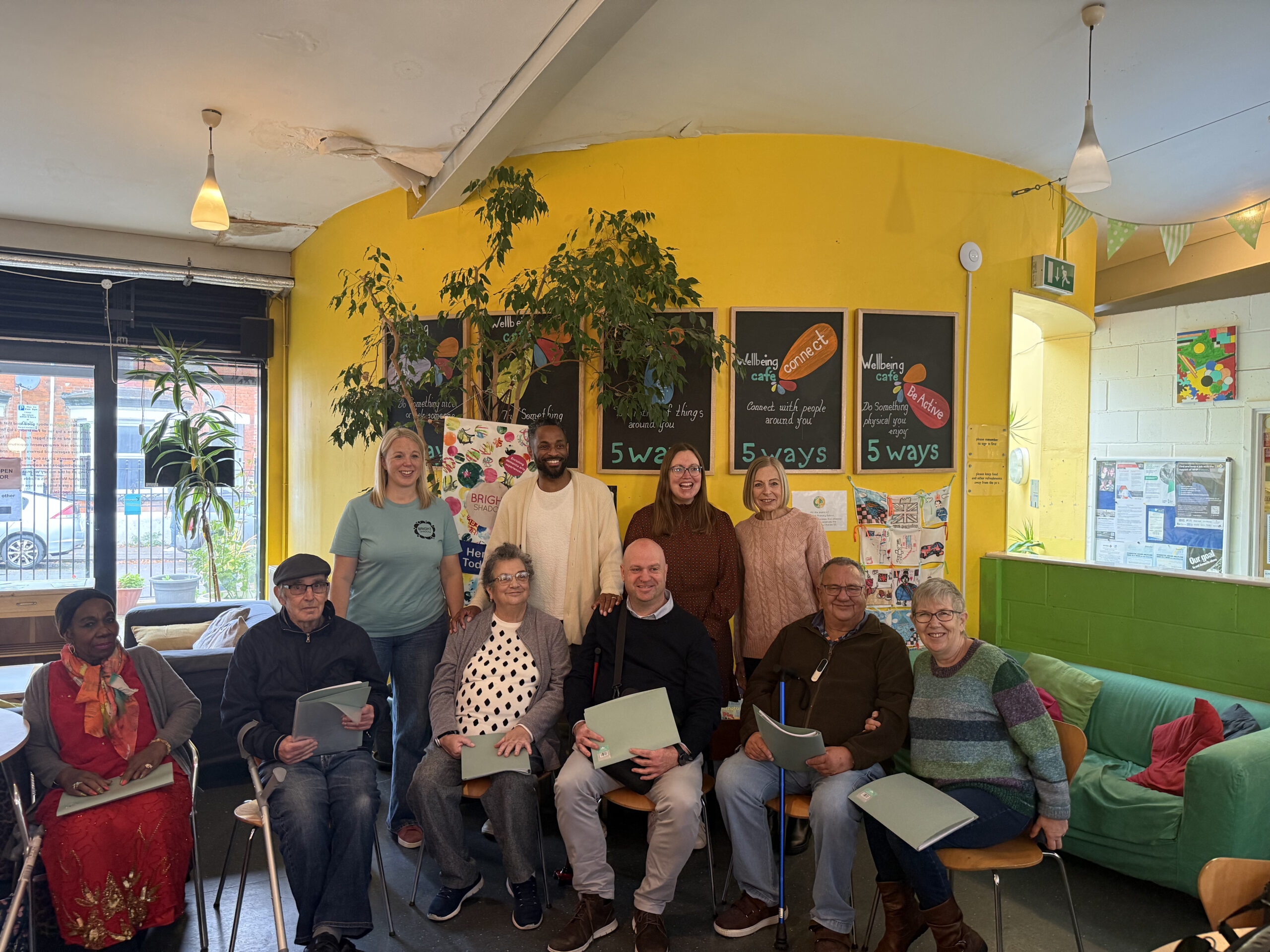 A group of people, a mix of seated and standing, are looking at the camera and smiling.