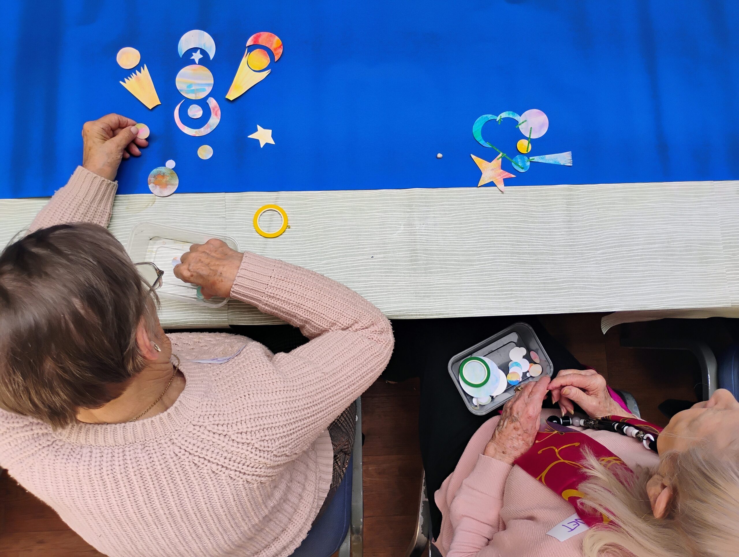 IMG_20250425_145816353_MP_AE A bird's eye view of two woman sitting at a blue table with painted paper planets and stars in front of them