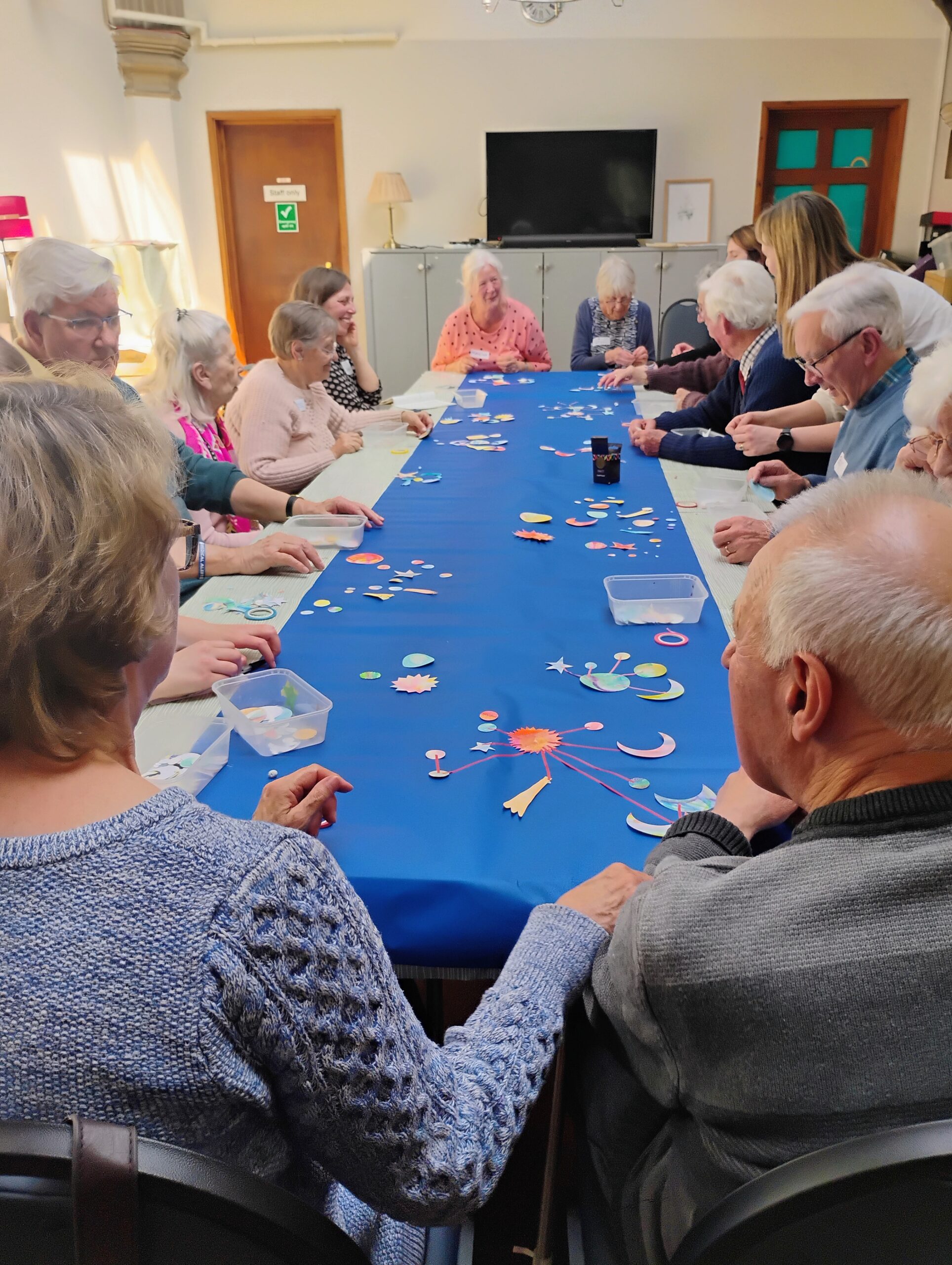 A group of people sit around a table with blue paper lining it. On the paper are the beginnings of individual collages based on the night sky